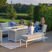 Family gathered around the Pulse 3 Seater Sofa Dining Set with Fire Pit, enjoying snacks and outdoor comfort, lead chine cushions featured.