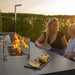 Mother and child enjoying a cosy moment around the Pulse 3 Seater Sofa Dining Set with Fire Pit, featuring a charcoal finish and a glowing fire pit with tempered glass surround.