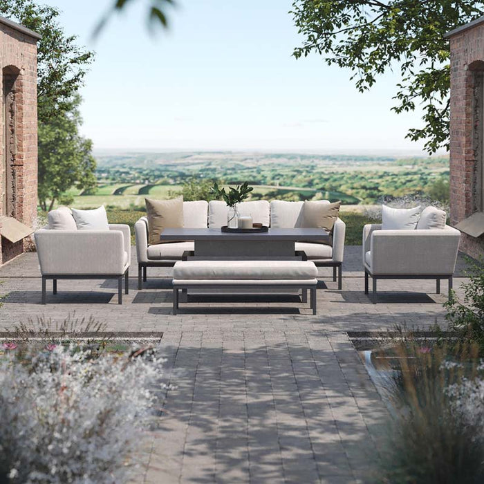 The Maze Pulse 3 Seater Sofa Dining Set in Oatmeal positioned in an elegant outdoor space, with the rising table in use and a scenic countryside view.