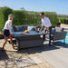 Two people effortlessly adjusting the height of the Pulse Rising Table in a stylish outdoor setting, showcasing the flexibility of the flanelle coloured dining set.