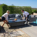 A man and woman adjusting the height of the rising table, demonstrating the practical feature of the Maze Pulse Dining Set.