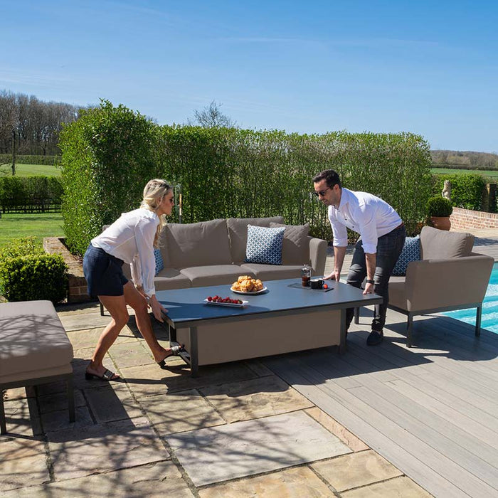 A couple adjusts the rising table’s height, showcasing the practical functionality of the Maze Pulse 3 Seater Sofa Dining Set in Taupe for dining or lounging outdoors.