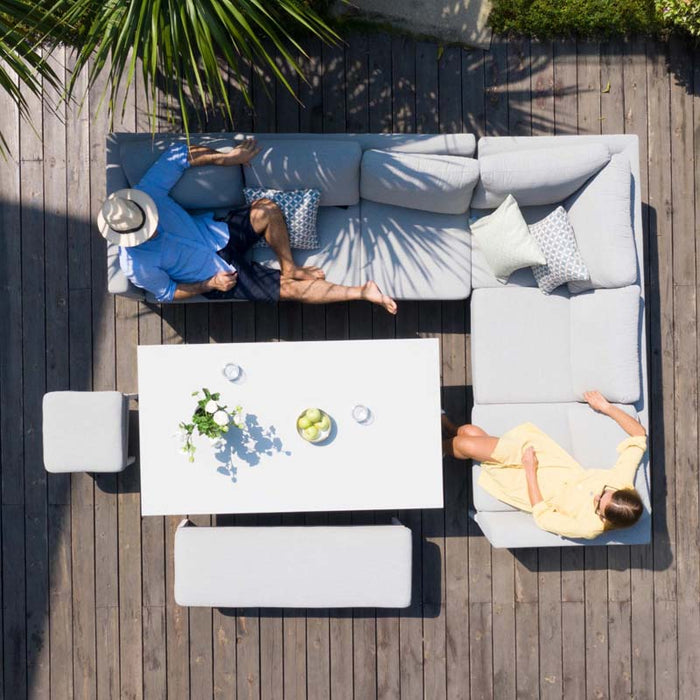 A couple enjoys a laid-back dining experience on a grey corner dining set with rising table, featuring soft cushions and a large table, set against a backdrop of vibrant garden foliage.