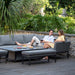 Comfortable couple lounging on the Pulse Left-Handed Rectangular Dining Set in flanelle, showcasing the spacious seating and stylish table in a lush garden.