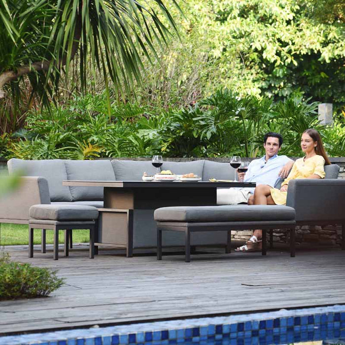 The Pulse Left-Handed Dining Set in flanelle with the table raised, as a couple enjoys an elevated dining experience in an inviting outdoor setting.