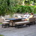 A couple relaxing on the Pulse corner dining set in taupe, enjoying a meal and drinks on the adjustable rising table, creating an inviting outdoor dining atmosphere.