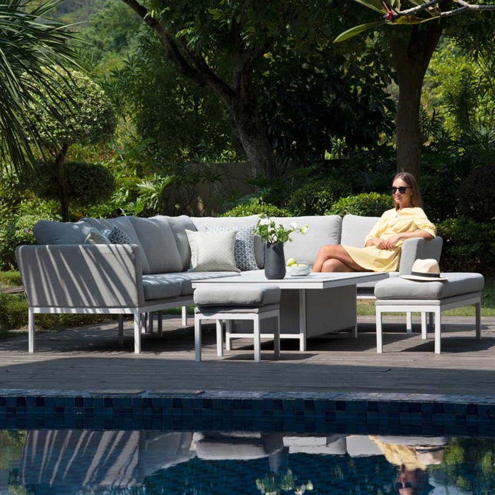 A woman lounges comfortably on the grey corner dining set, illustrating its spacious design and the versatility of the rising table feature.