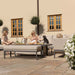 A peaceful moment of a woman enjoying her outdoor space on the Pulse left-handed corner dining set in oatmeal, relaxing with her dog beside the adjustable rising table.