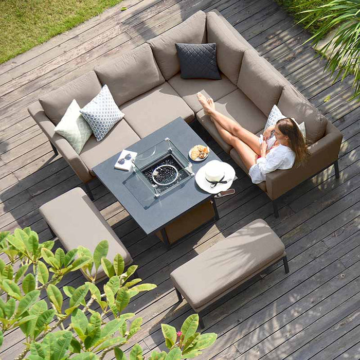 A relaxed lifestyle image showing the Maze Pulse Square Corner Dining Set with Fire Pit in taupe from above, featuring a woman lounging and enjoying a serene outdoor moment.