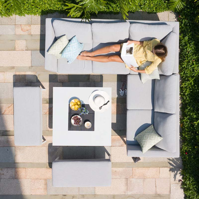 Bird's-eye view of Pulse Square Corner Dining Set with Rising Table in lead chine, woman relaxing on sofa with cushions, and table set with refreshments.