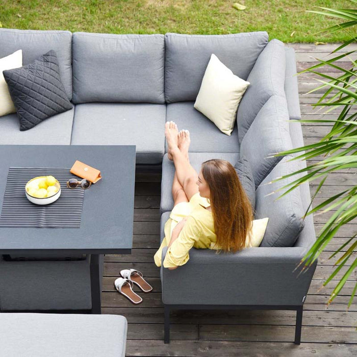 Woman seated on the Pulse Square Corner Dining Set with Rising Table in flanelle, enjoying outdoor relaxation.