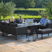 A group of people enjoying the outdoors on the Pulse U Shape Corner Dining Set in charcoal, with a modern fire pit and elegant lanterns adding warmth and style to the patio setting.