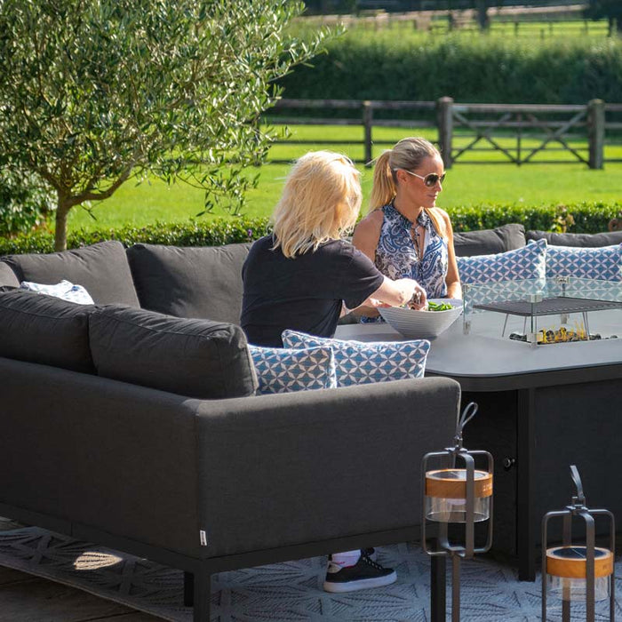 Two women enjoy a relaxing outdoor meal on the charcoal Pulse U Shape Corner Dining Set, featuring a fire pit at the centre, providing both warmth and style.