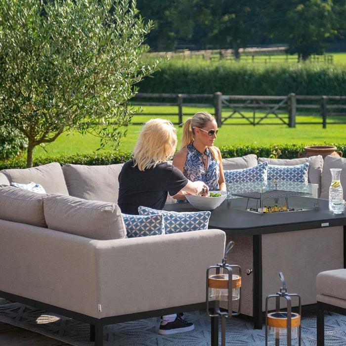 Two women enjoying an outdoor meal on the Pulse U Shape Corner Dining Set in taupe, featuring a sleek fire pit at the centre, perfect for casual dining and lounging.