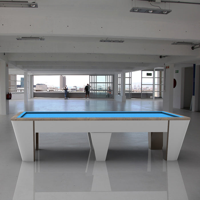 MBM Biliardi Quantum pool table with light oak finish and electric blue felt, placed in a minimalist industrial-style space with panoramic views.