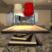 An MBM Biliardi Ziggurat pool table with a light wood frame and black accents, under unique art deco style pendant lamps in a modern room.