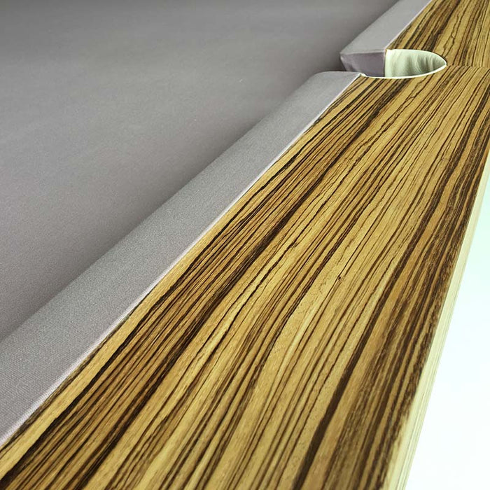 Close-up of an MBM Biliardi Ziggurat pool table pocket with pool balls near the edge, showing the wood, cream leather, and lilac felt.