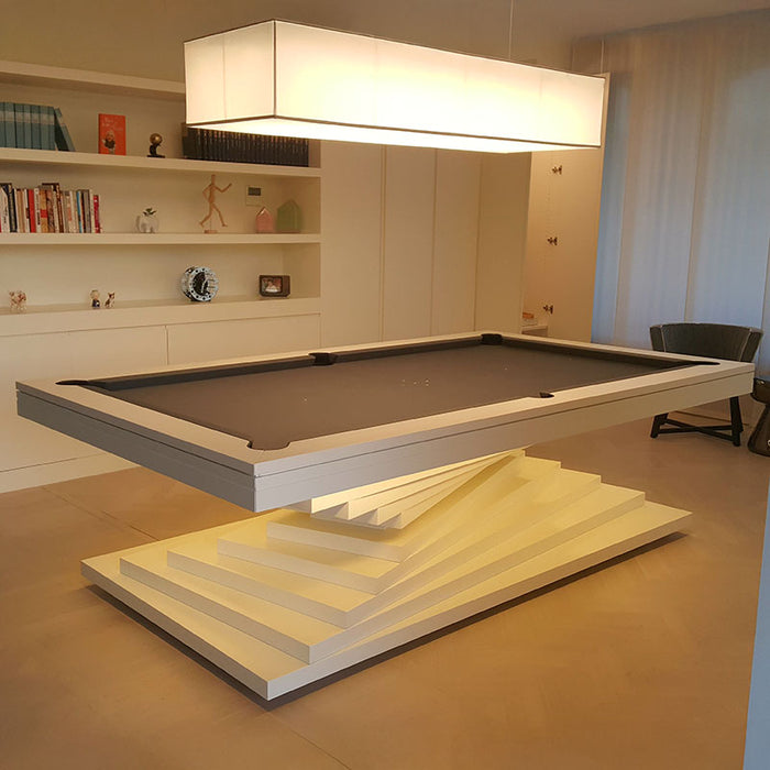 A white MBM Biliardi Ziggurat pool table with a gray felt surface, in a modern and minimalist interior setting with built-in shelving.