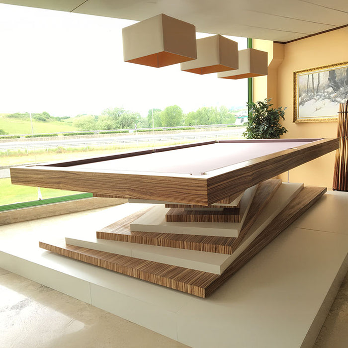 A modern MBM Biliardi Ziggurat pool table with a wood and white layered base, bathed in natural light from large windows overlooking a green landscape.