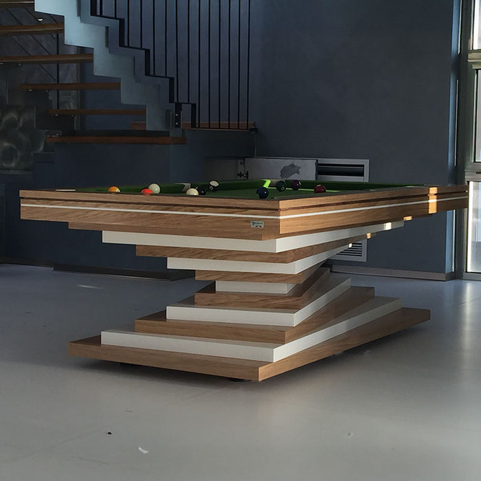 An MBM Biliardi Ziggurat pool table showcasing its wood and white layers, set in a modern space with a staircase in the background.