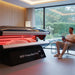 MXP PowerBed Pro 100 red light therapy session in progress, showing a relaxed user inside the open pod and a companion seated nearby in a peaceful spa environment.