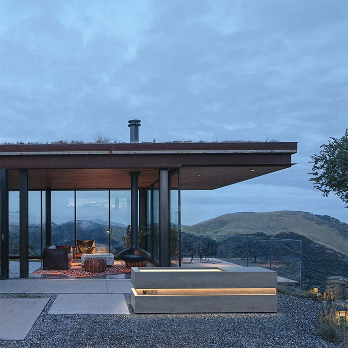 Elegant Nordic Vitality LOKI Ice Bath placed in a remote hillside retreat with panoramic views, modern glass architecture, and warm ambient lighting for a tranquil spa experience.