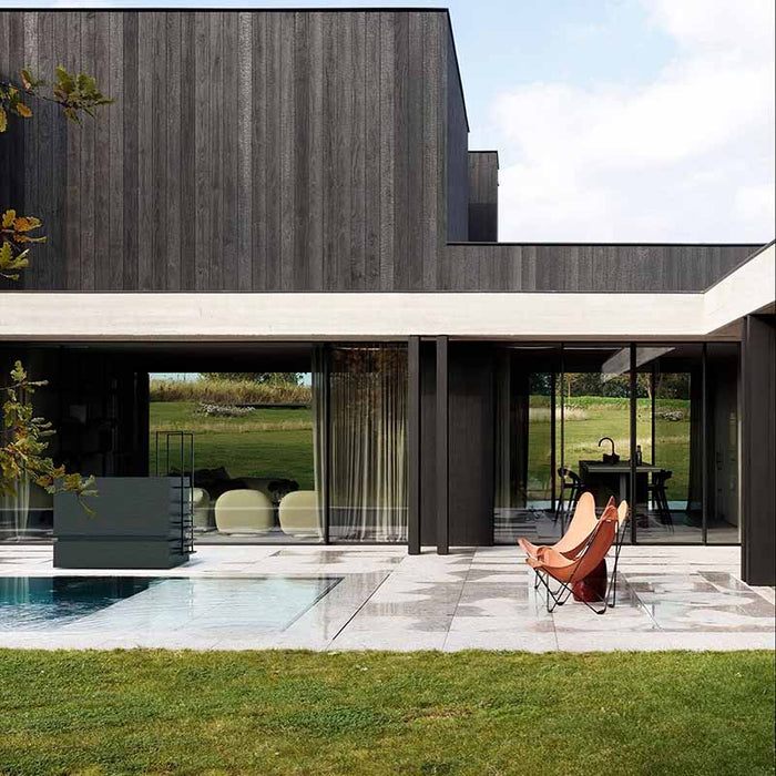 Nordic Vitality THOR Ice Bath in Ardesia Nero finish placed next to a pool at a minimalist dark-panelled home with open lawn backdrop.