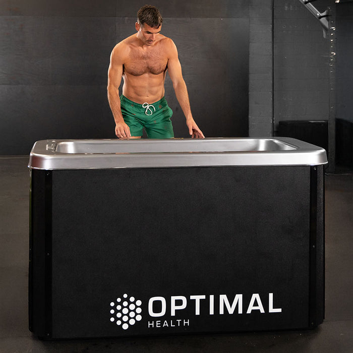 A muscular athlete stands beside the Optimal Health Ice Bath, preparing for an intense yet refreshing cold therapy session to enhance performance.