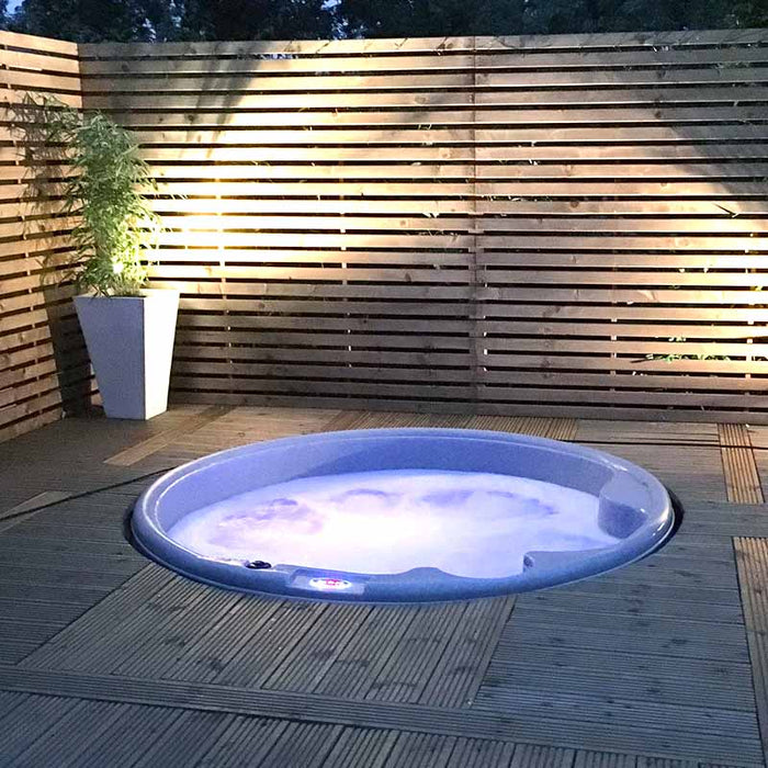 Built-in light grey spa tub in a wooden deck area at dusk.