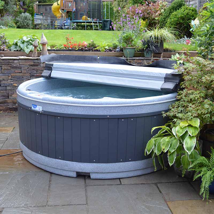 Covered grey hot tub in a garden setting with lush greenery.