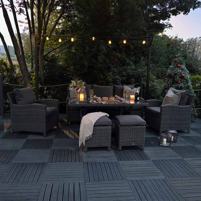 Paris 7 Seater Deluxe Sofa Dining Set arranged in a cosy evening garden setting, illuminated by string lights. The grey wicker furniture with soft cushions and lanterns creates a warm, inviting atmosphere.