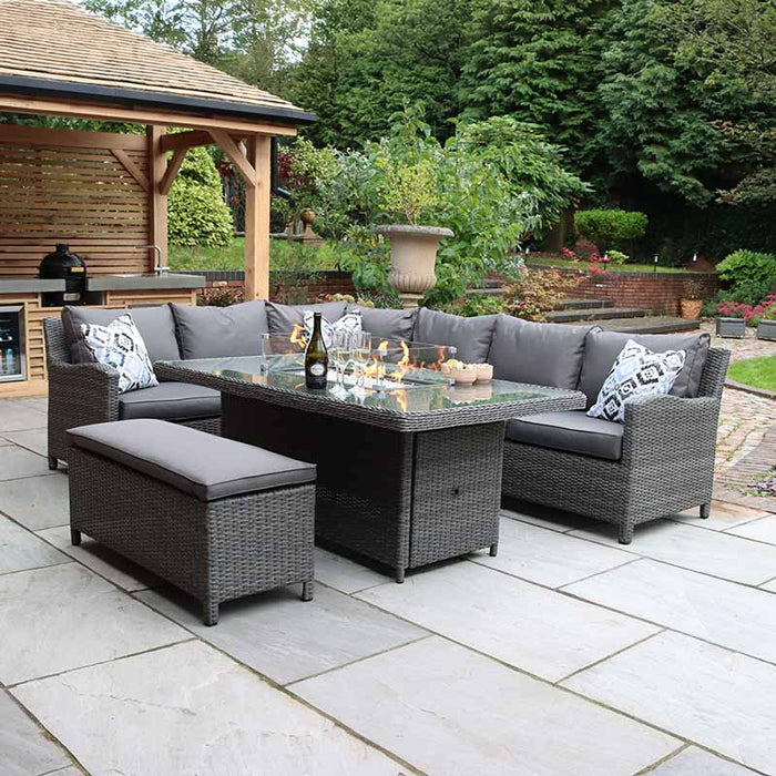 A cosy outdoor setting featuring the Paris Fire Pit Corner Dining & Lounge Set with a rectangular glass-top table, showcasing its elegant rattan weave and comfortable grey cushions.