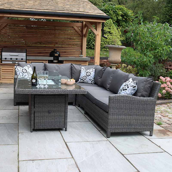 The Paris Fire Pit Corner Dining & Lounge Set with Rectangular Table elegantly arranged in a garden, perfect for intimate outdoor gatherings.