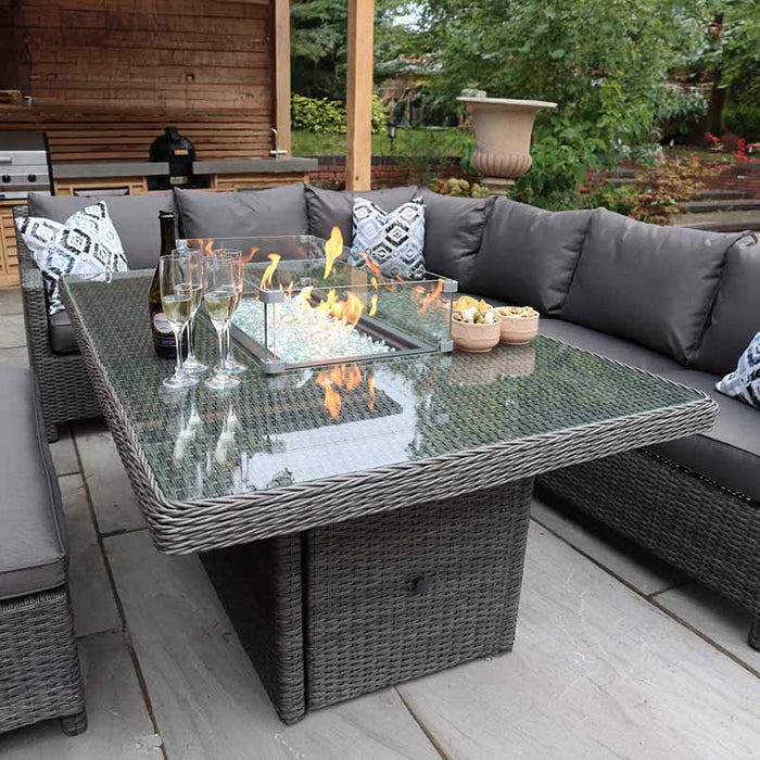 A detailed view of the Paris Fire Pit Corner Dining & Lounge Set's rectangular table, featuring a built-in fire pit and glassware, creating a luxurious outdoor dining experience.