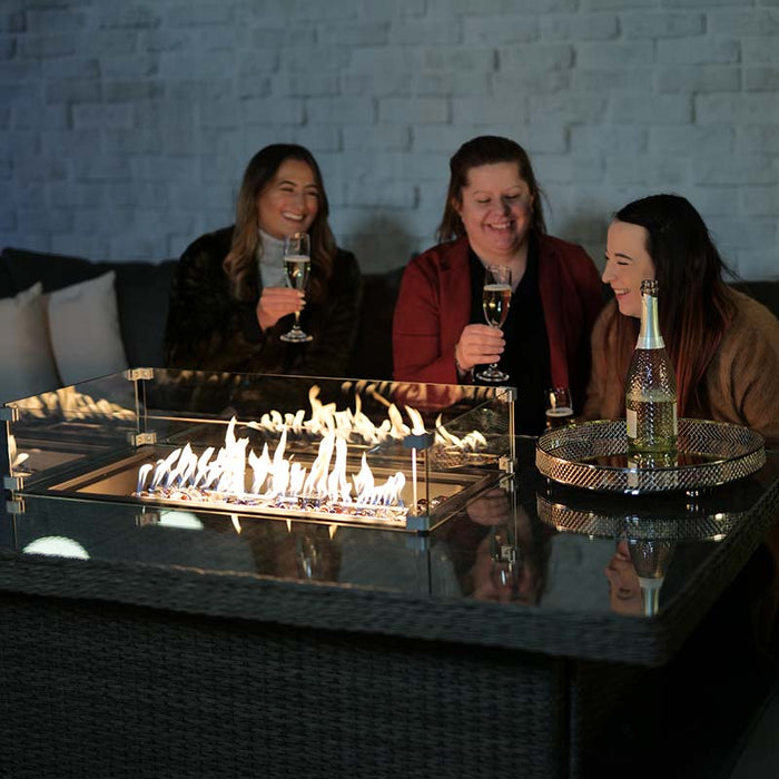 A group of women enjoying drinks around the Paris Fire Pit Corner Dining & Lounge Set, with the fire pit providing a warm, glowing centrepiece.