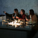 Three women sharing a laugh while taking a selfie around the Paris Fire Pit Corner Dining & Lounge Set, the fire pit creating a cosy ambiance.