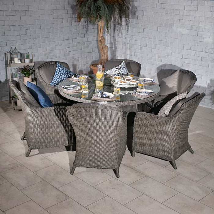 The Paris Imperial Round Dining Set arranged indoors, featuring a round glass-topped table and grey rattan chairs with cushions, perfect for elegant dining.