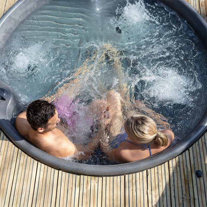  Two people relaxing in a bubbling outdoor round hot tub.