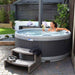  Woman reading in a garden hot tub with steps and towels nearby.