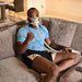 ReOxy Hypoxic Therapy Device in use, man in blue t-shirt seated on sofa with raised fist wearing full face breathing mask and finger pulse oximeter, living room setting.