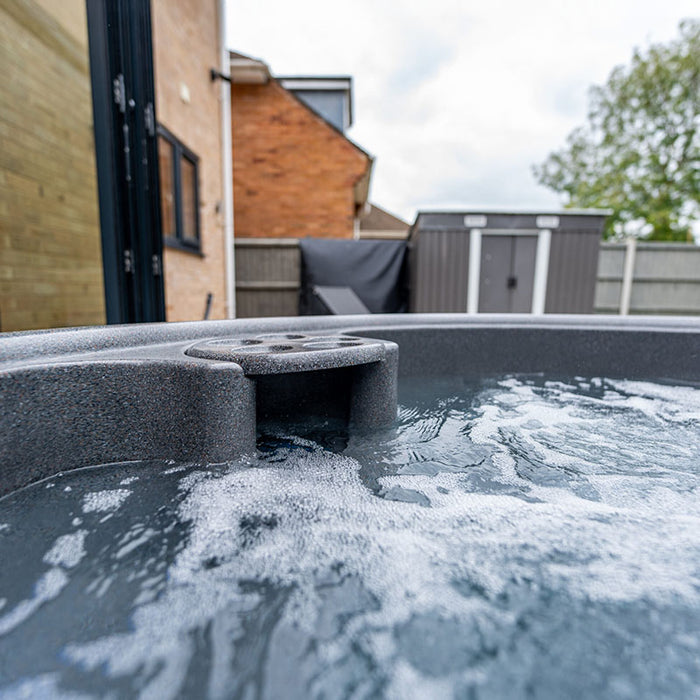 Close-up of Rotospa Orbis Hot Tub showing bubbling water and integrated cup holders for outdoor spa relaxation.