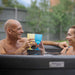 Happy couple toasting with colourful glasses while relaxing in Rotospa Orbis Hot Tub.