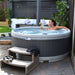 Woman relaxing in Rotospa Orbis Hot Tub reading a book in a stylish backyard garden setup.