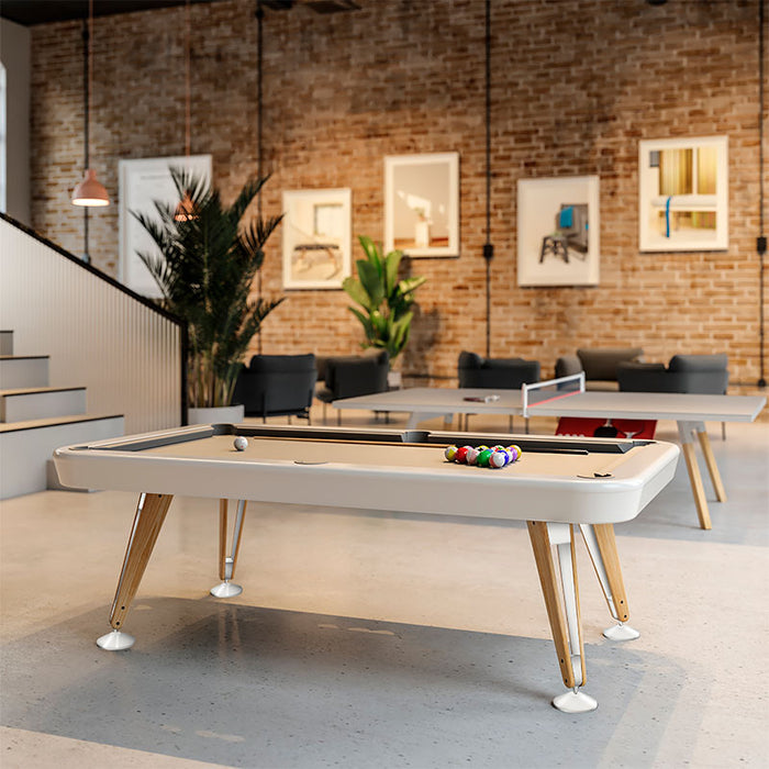 RS Barcelona Diagonal pool table with white frame and wooden legs placed in a modern loft interior with exposed brick walls, large windows and contemporary lounge seating.