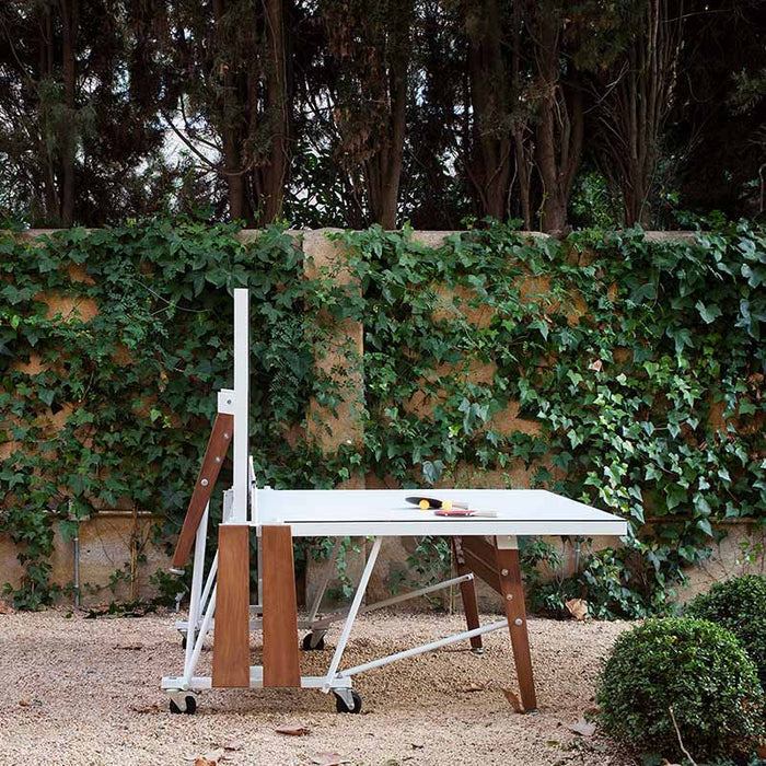 Folded RS Barcelona ping pong table in vertical position with compact storage design, wooden panels and wheels for easy movement outdoors.