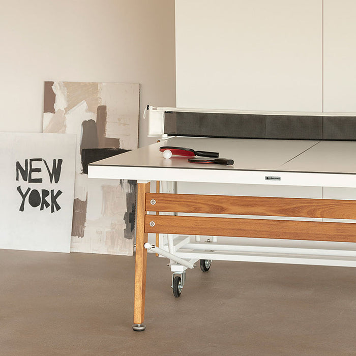 RS Barcelona folding table tennis table detail showing smooth white playing surface, wooden frame and net with paddles and ball for indoor ping pong use.