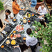 RS Barcelona RS Max dining football table in outdoor patio with guests gathered around, glass tabletop filled with food and drinks, luxury social dining and entertainment table.