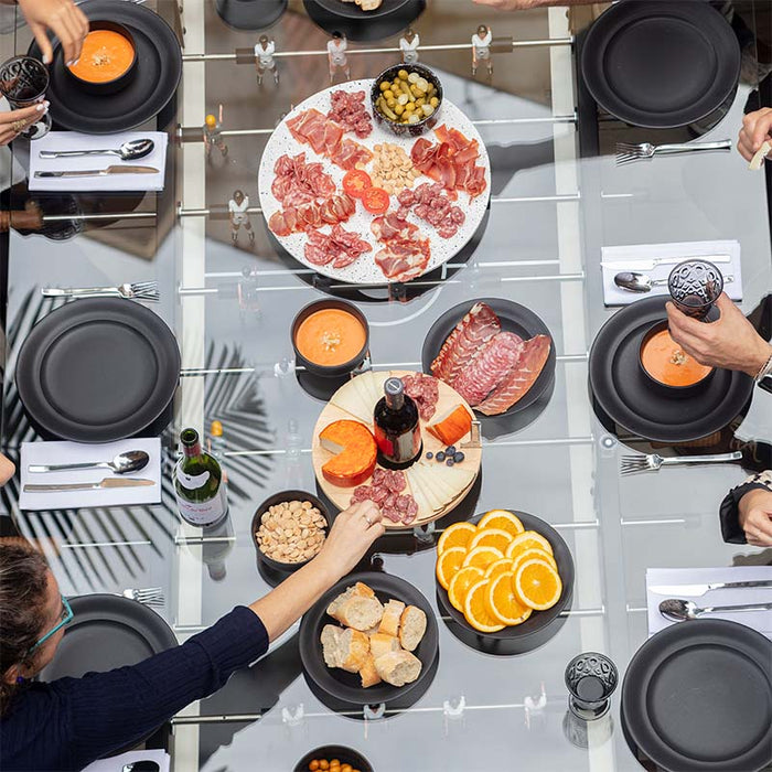 Overhead view of RS Barcelona RS Max dining football table with people dining, sharing food and drinks, stylish glass surface with integrated foosball game for social gatherings.