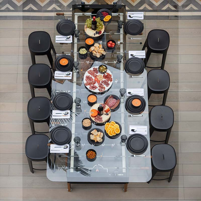 Overhead view of RS Barcelona RS Max dining football table fully set for dining with plates, food and stools, luxury glass dining table with integrated foosball game design