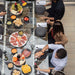 Top view of RS Barcelona RS Max dining football table with glass surface, people dining with gourmet food and wine, multifunctional foosball dining table for social gatherings.